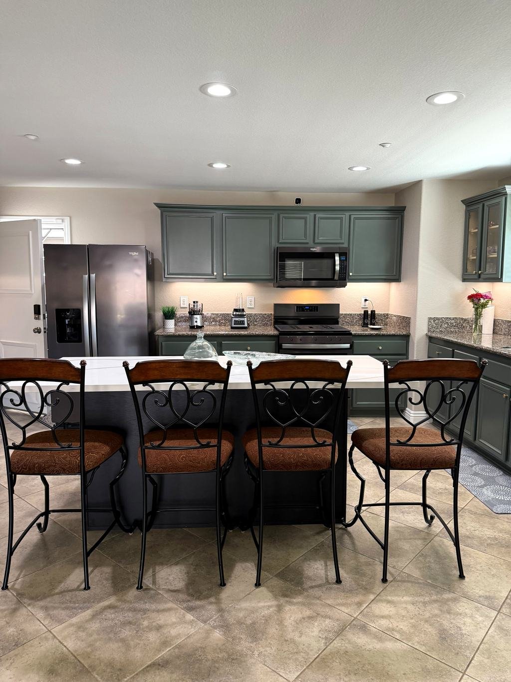 Kitchen with green cabinets, granite counters and island