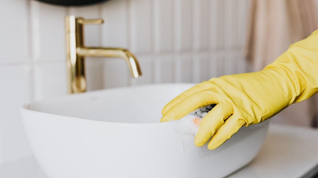 Gloved hand scrubbing a white bathroom sink